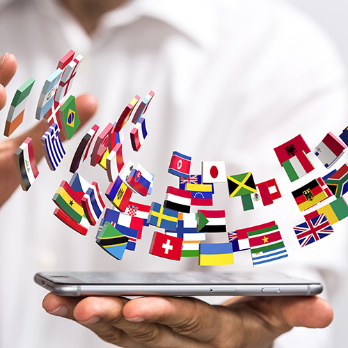 Viele Flaggen der Welt sowie ein Handy symbolisieren die sprachliche Bandbreite des Online-Übersetzungsservices von ClickTranslate. 